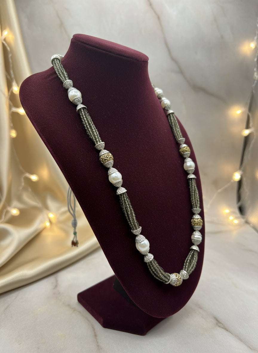 The set of jewellery featuring a long necklace with grey-coloured glass beads and metallic accents, paired with matching earrings, displayed on a mannequin bust.