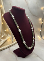 The set of jewellery featuring a long necklace with grey-coloured glass beads and metallic accents, paired with matching earrings, displayed on a mannequin bust.