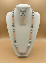The set of jewellery featuring a long necklace with peach-coloured glass beads and metallic accents, paired with matching earrings, displayed on a mannequin bust. Party wear set.