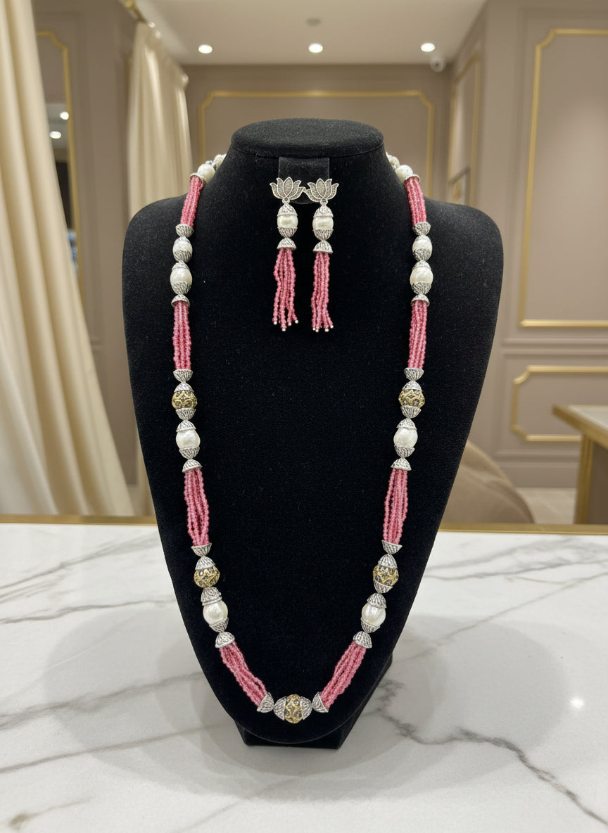 The set of jewellery featuring a long necklace with pink-coloured glass beads and metallic accents, paired with matching earrings, displayed on a mannequin bust.