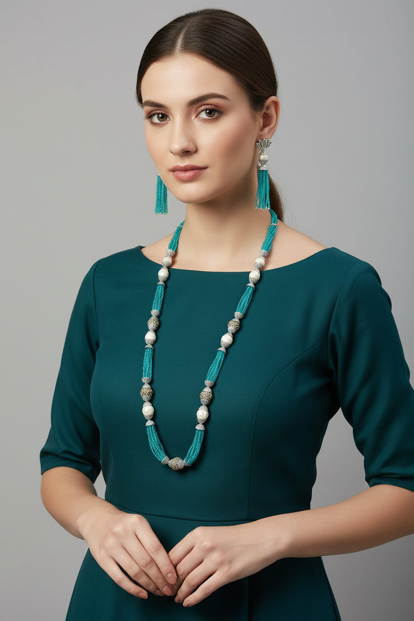 The set of jewellery featuring a long necklace with sky blue-coloured glass beads and metallic accents, paired with matching earrings, displayed on a mannequin bust. Party wear set.
