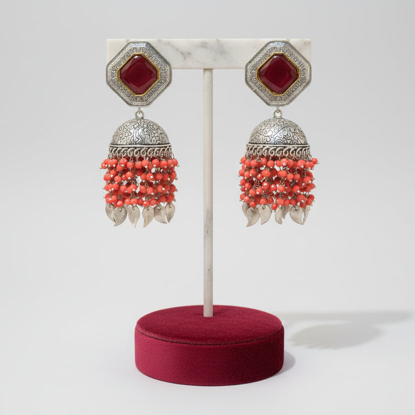These earrings carries the redstone in the top stud and carrot red hangings underneath the Jhumkey dome and nano oxidised hanging in in the last.