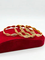 A set of four three-tone micro gold-plated copper bangles featuring a repeating floral eyelet and lattice design in yellow, white, and pink gold finishes, displayed on a red velvet jewelry stand.