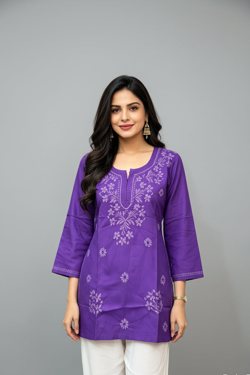 Front-facing view of a woman wearing a royal purple cotton short kurti featuring delicate white floral embroidery, a keyhole neckline, and a square hem line, paired with white trousers.
