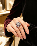 Silver-tone floral halo ring with violet purple stones and sparkling AD center, worn on hand at luxury jewelry boutique.