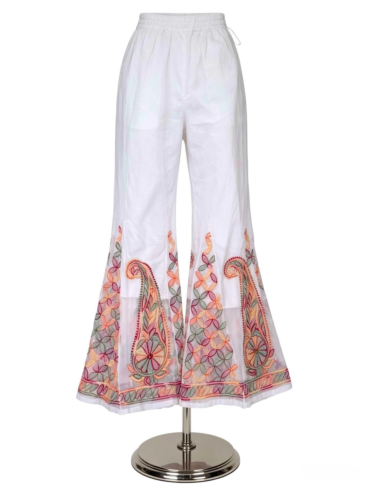 A professional studio product listing shot of white semi-georgette sharara pants displayed on a silver mannequin stand against a solid white background, showcasing the soft flowy drape, elastic waistband, and a sheer organza bottom border with multi-hued embroidery.