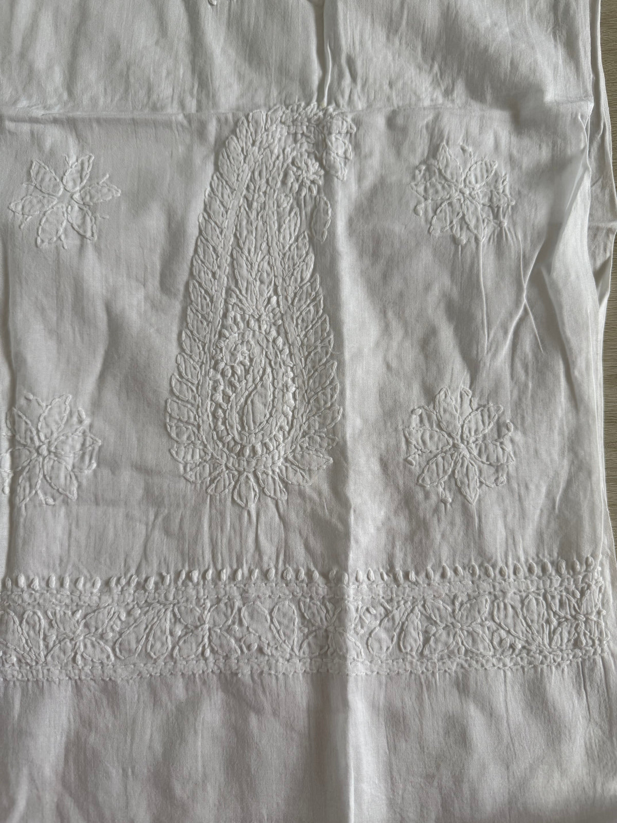 White embroidered cotton fabric with a central paisley motif, floral motifs, and a decorative lace-like band near the top.