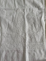 White embroidered cotton fabric with a central paisley motif, floral motifs, and a decorative lace-like band near the top.