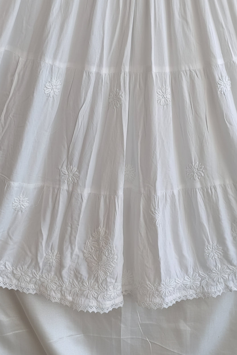 White tiered skirt with delicate floral embroidery and lace trim along the hem, shown hanging against a dark background.