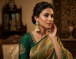 Woman in a green and gold saree with jewellery in an ornate room.