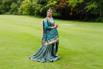 Woman in traditional attire standing on a grassy field with trees in the background