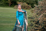 Woman in traditional attire standing outdoors with greenery in the background