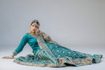 Woman in traditional bridal gharara outfit with floral patterns sitting on grass