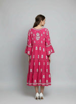 Woman is posing this rear view of this hot pink dress with white floral patterns in a neutral setting.