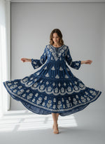 Woman is wearing a navy blue colour dress with white floral patterns in a neutral setting.