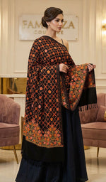 Woman wearing a black and orange patterned shawl in an elegant room.