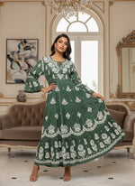 Woman wearing a bottle green colour dress with white floral patterns in a neutral setting.