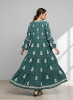 Woman wearing a green colour dress with white floral patterns in a neutral setting.