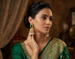 Woman wearing a green saree with gold embroidery, posing indoors.