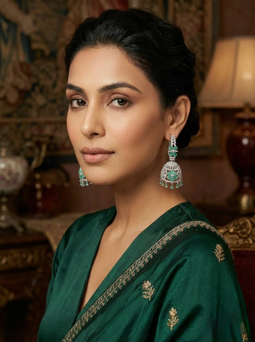 Woman wearing a green saree with intricate patterns and matching earrings in an ornate room.