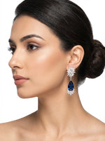 Woman wearing a pair of earrings with a blue gemstone on a white background