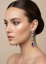 Woman wearing a pair of earrings with blue gemstones against a beige background