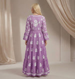 Woman wearing a purple dress with white floral patterns in a neutral setting.