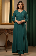 Woman wearing a teal dress with intricate patterns in a room with a mirror and green curtains.