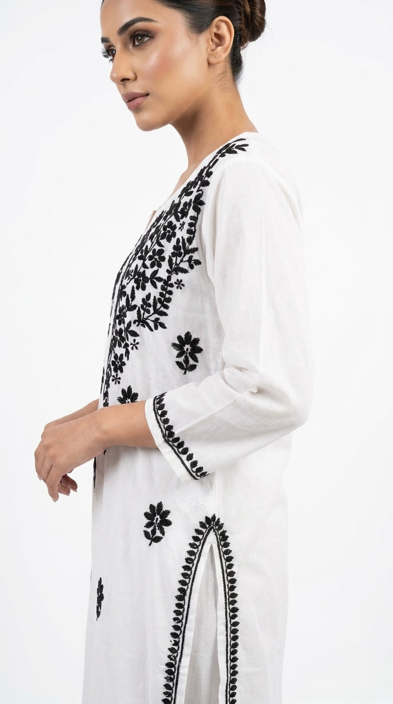 Woman wearing a white outfit with black floral embroidery on a white background