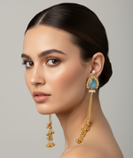 Woman wearing gold earrings with blue gemstones against a grey background