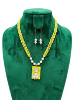 Yellow beaded necklace with a rectangular pendant and matching earrings on a green velvet stand.