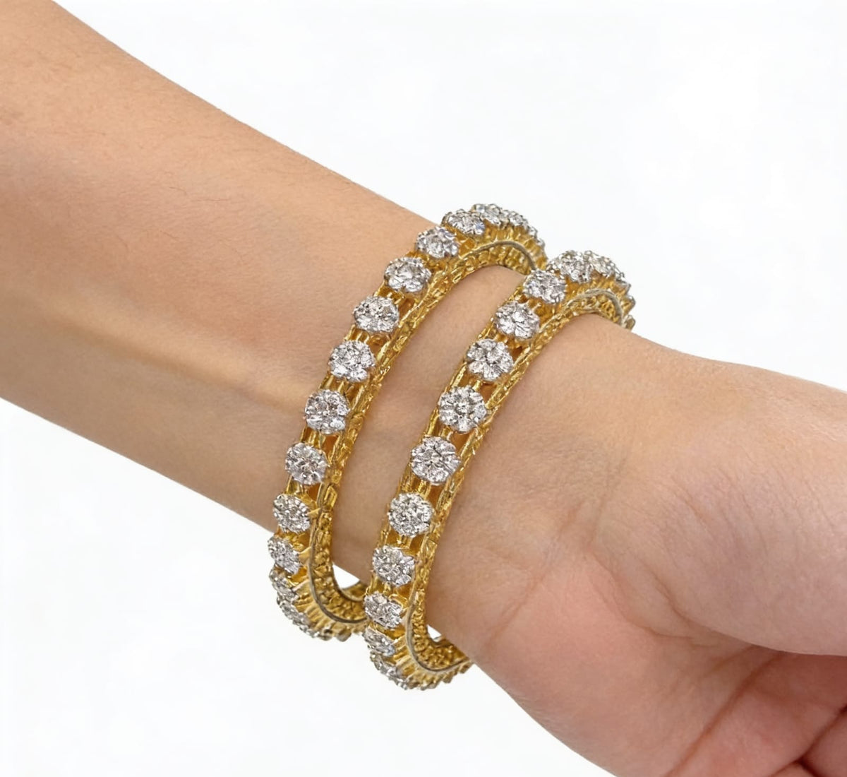 Pair of gold-plated bangles featuring a delicate honeycomb lattice design adorned with floral-shaped American Diamond clusters, shown on a model's wrist with a clean white background.