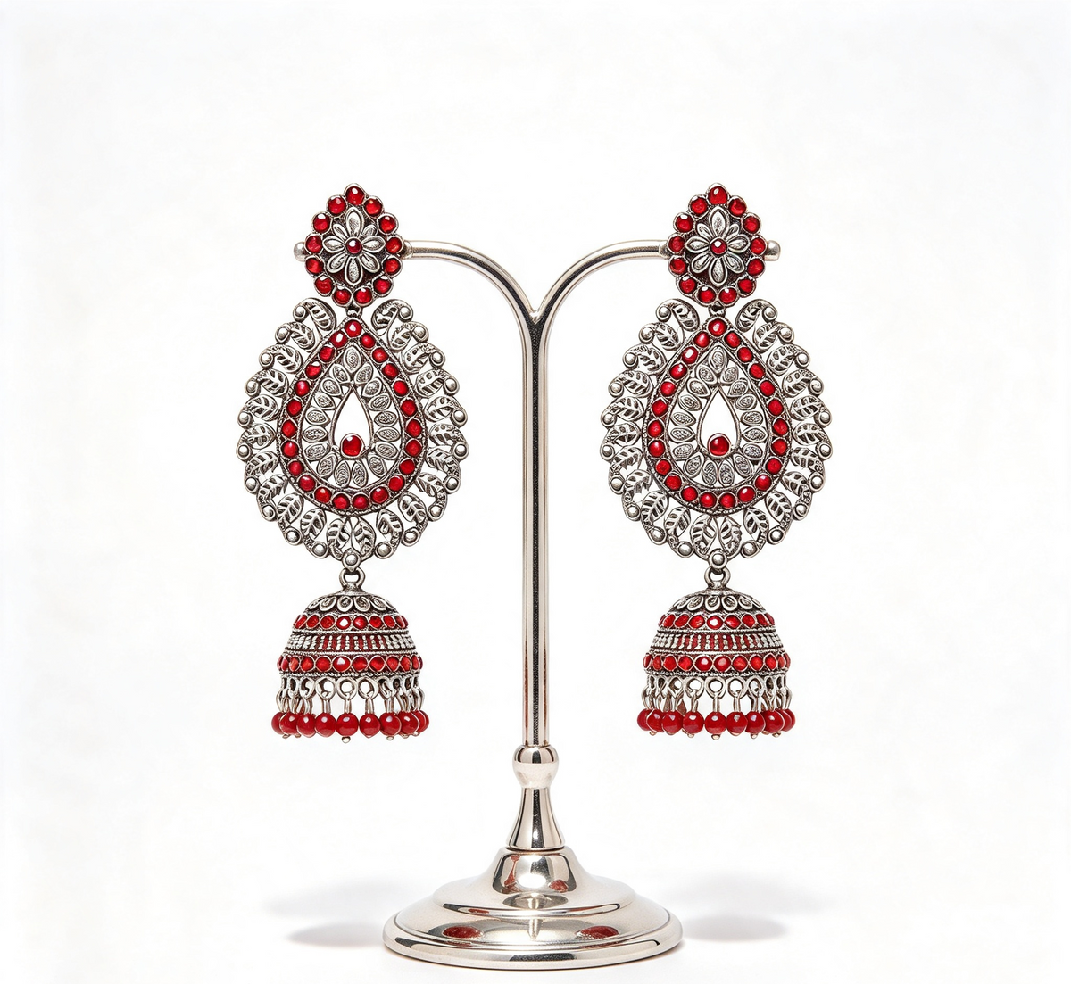 a pair of oxidised tone tear drop earrings with red nano stones and hangings are displayed on a silver stand.