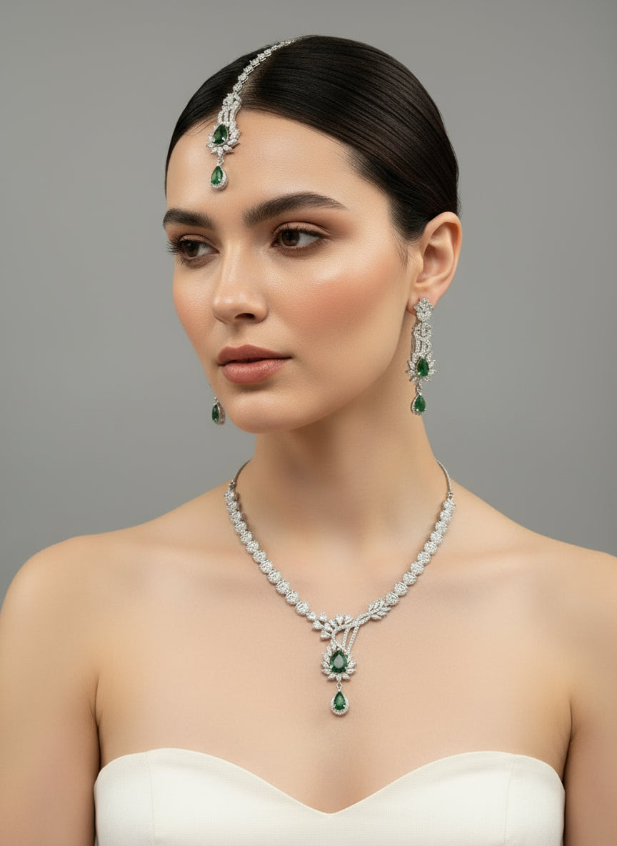 a rhodium-plated brass jewellery set with American diamond and emerald green central stone semi-precious stones, including a necklace, earrings, and maang tikka by famaza couture