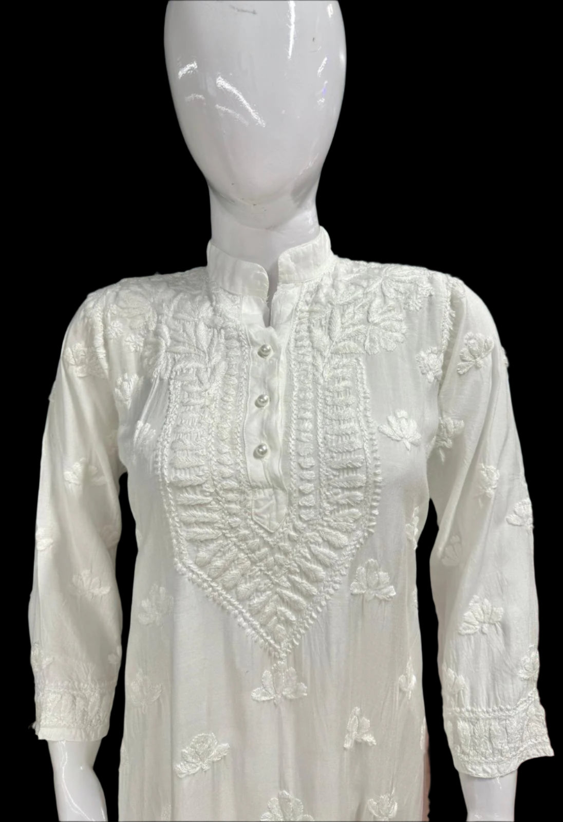 A white Chikankari short kurti displayed on a mannequin, featuring intricate hand embroidery with floral motifs.
