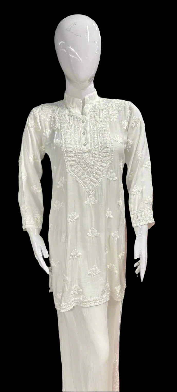 A white Chikankari short kurti with collar and buttons, featuring intricate hand embroidery with floral motifs.