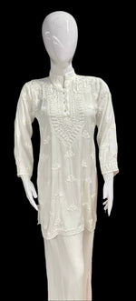 A white Chikankari short kurti with collar and buttons, featuring intricate hand embroidery with floral motifs.