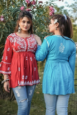 Two women wearing red and blue traditional outfits standing outdoors.