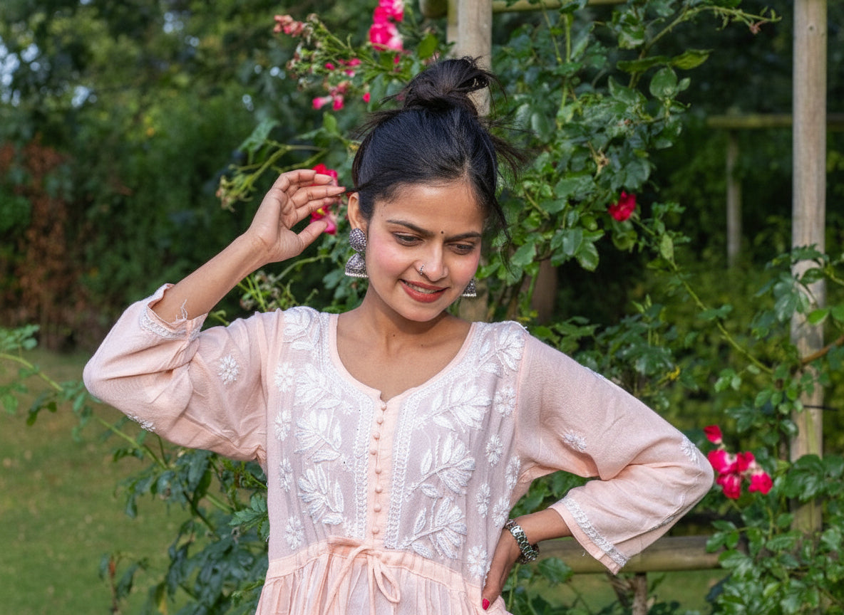 A woman standing outdoors wearing a short frock style kurti with embroidery and a tie-up waist, in a garden