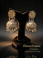 Dual-tone kundan jhumka earrings on a black stand, with gold-tone stone settings, embossed domes and dangling metal drops.