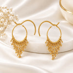 Pair of 22K gold-plated beaded tassel hoop earrings displayed on elegant wooden and gold stand, dark wood interior background — luxury Pakistani jewellry.