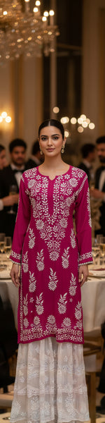 Woman wearing a pink embroidered traditional outfit in an elegant indoor setting.