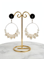 Ivory white shell-shaped dangle hoop earrings with faux pearls on a gold-tone display stand.
