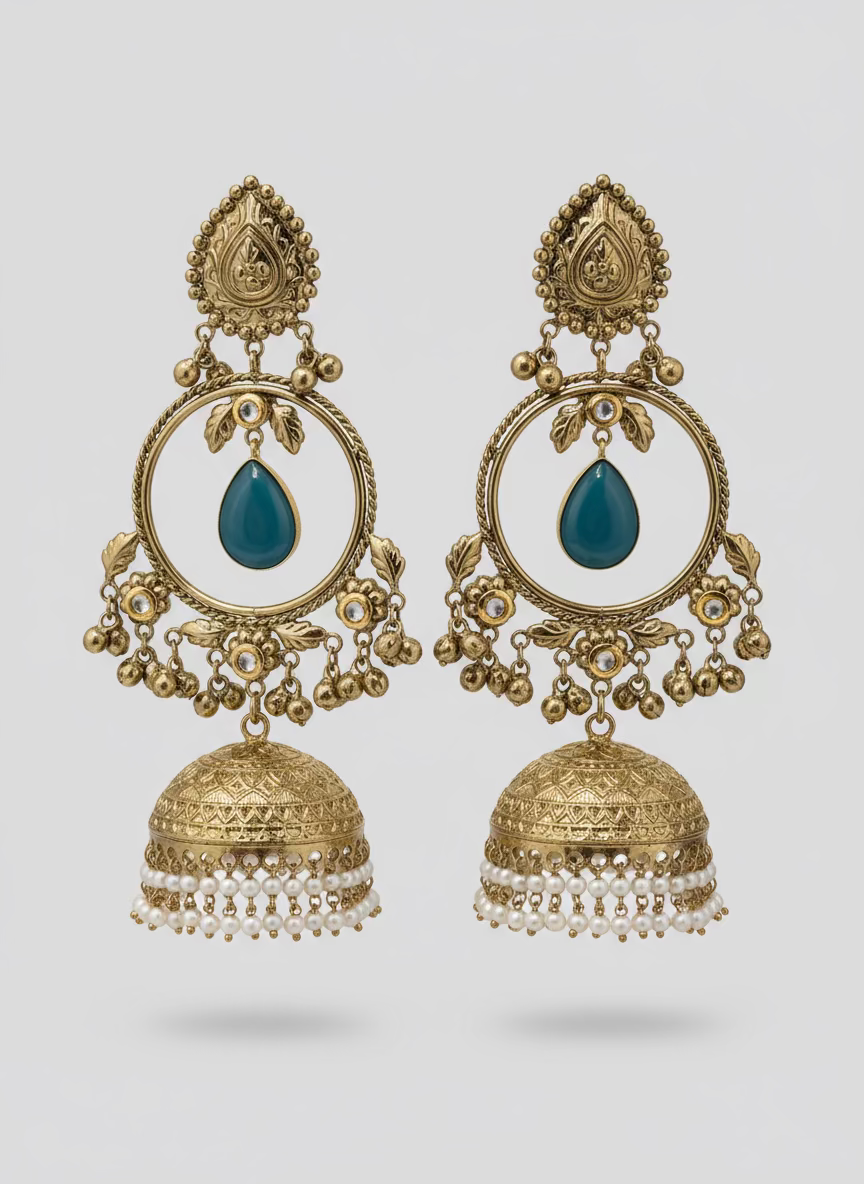 Ornate gold earrings with black stones and pearl-like beads on a textured surface.