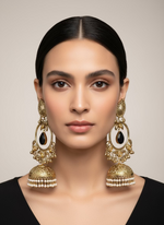 Gold and black stone earrings with dangling elements held by a hand, with a display of similar earrings in the background.