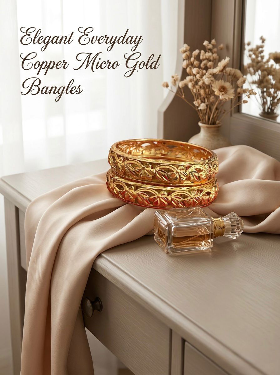 A set of two micro gold-plated copper bangles with an intricate, open-work floral and vine pattern, elegantly displayed on a champagne-colored silk cloth next to a glass perfume bottle on a light wooden vanity.