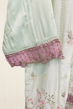 Close-up of a mint green sleeve with openwork trim and a pink floral embroidered scalloped cuff