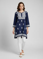 model is wearing and posing in this navy blue colour short length Chikankari kurti with white floral hand embroidery with white jeans