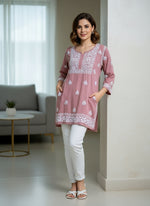 model is wearing and posing in this tea pink colour short length Chikankari kurti with white floral hand embroidery with white jeans