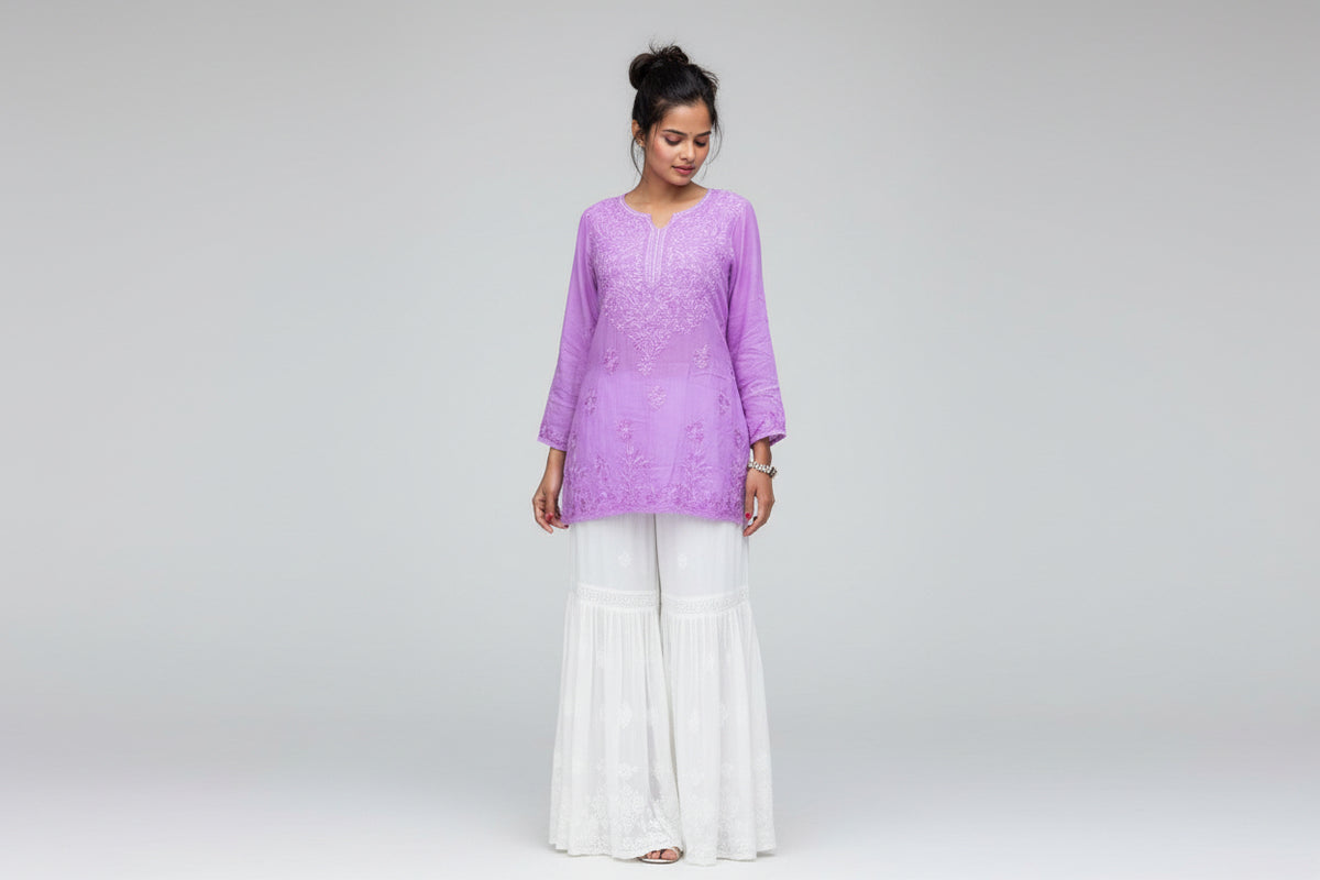 model is wearing purple short chikankari embriodery kurti with white hand embrioderd flared trousers in queens garden in london